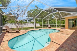 Una piscina techada con suelo de ladrillo, dos sillas reclinables y un cerramiento de vidrio.