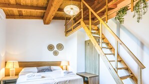 A bedroom with a wooden staircase, a bed with white linens, two bedside lamps, and wall decor. - Da Lisa by Interhome (Cecina)