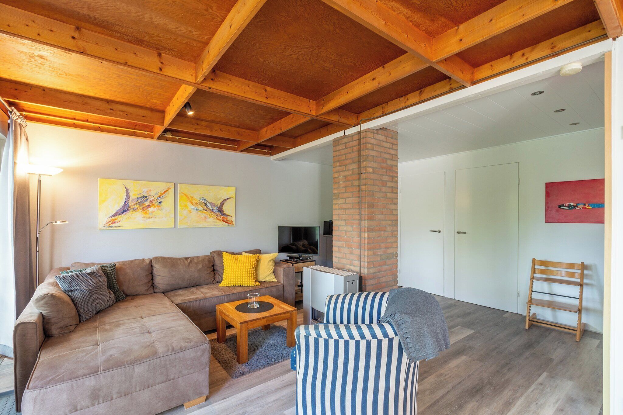 Un salon chaleureux avec un canapé d’angle marron, un fauteuil à rayures, une petite table basse en bois et un téléviseur.