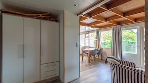 A spacious room with a large wardrobe, a dining area with a table and chairs, and a cozy seating area with striped cushions.