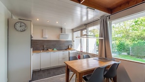 A modern kitchen with white cabinets, a wooden dining table, and a clock on the wall.