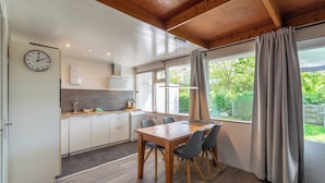 A modern kitchen with wooden cabinets, a dining table with chairs, and a large window with curtains.