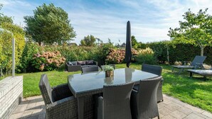 Un patio con un tavolo rotondo e sedie, immerso nel verde e con un'alta stele nera.