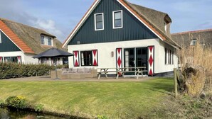 A traditional Dutch house with a steep gable roof, a wooden bench, and a small pond in the foreground. - Villa in Callantsoog with Whirlpool and Beach (Callantsoog)