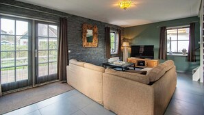 A modern living room with a sectional sofa, a TV, and a fireplace. - Villa in Callantsoog with Whirlpool and Beach (Callantsoog)
