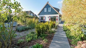 A house with a sloped roof, a brick pathway leading to the entrance, and a garden with various plants and shrubs.