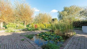 A garden with a pond, brick pathway, and various plants.
