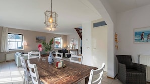 A dining area with a wooden table, white chairs, and a hanging light fixture. - Villa in Callantsoog near the Beach (Callantsoog)