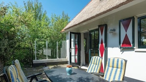 An outdoor seating area with a table and chairs, a thatched roof, and a white building with large windows and red triangular decorations. - Villa in Callantsoog near the Beach (Callantsoog)