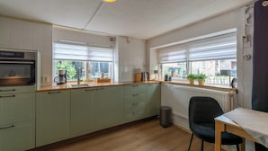 A kitchen with light green cabinets, a wooden countertop, a black chair, and a table with a lamp. - Holiday Home in Callantsoog near Beach (Callantsoog)