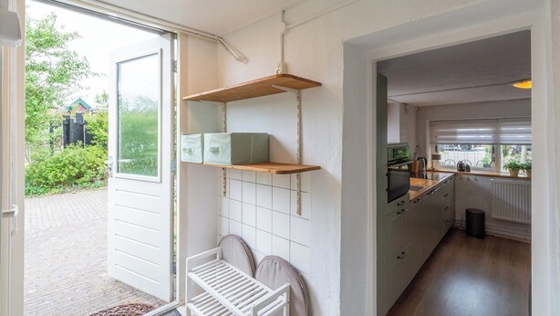 A kitchen with white cabinets, a wooden shelf, and a view of the garden. - Holiday Home in Callantsoog near Beach (Callantsoog)