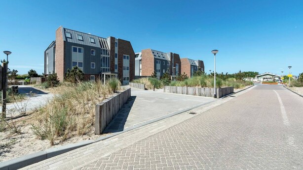 Ein modernes Gebäude mit flachem Dach und großen Fenstern, umgeben von einem gepflasterten Gehweg und etwas Vegetation.