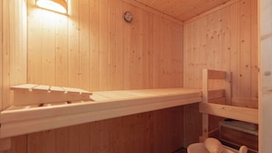 Eine Holzsauna mit einer Bank, einer Wanduhr und einem Holzeimer mit Wasserschöpflöffel.