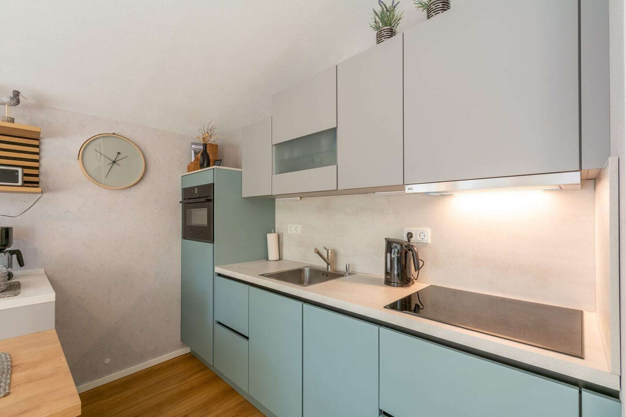 Ett modernt kök med ljusblå skåp, en diskho i rostfritt stål och en inbyggd ugn. Det finns en klocka på väggen och en liten växt på bänkskivan.