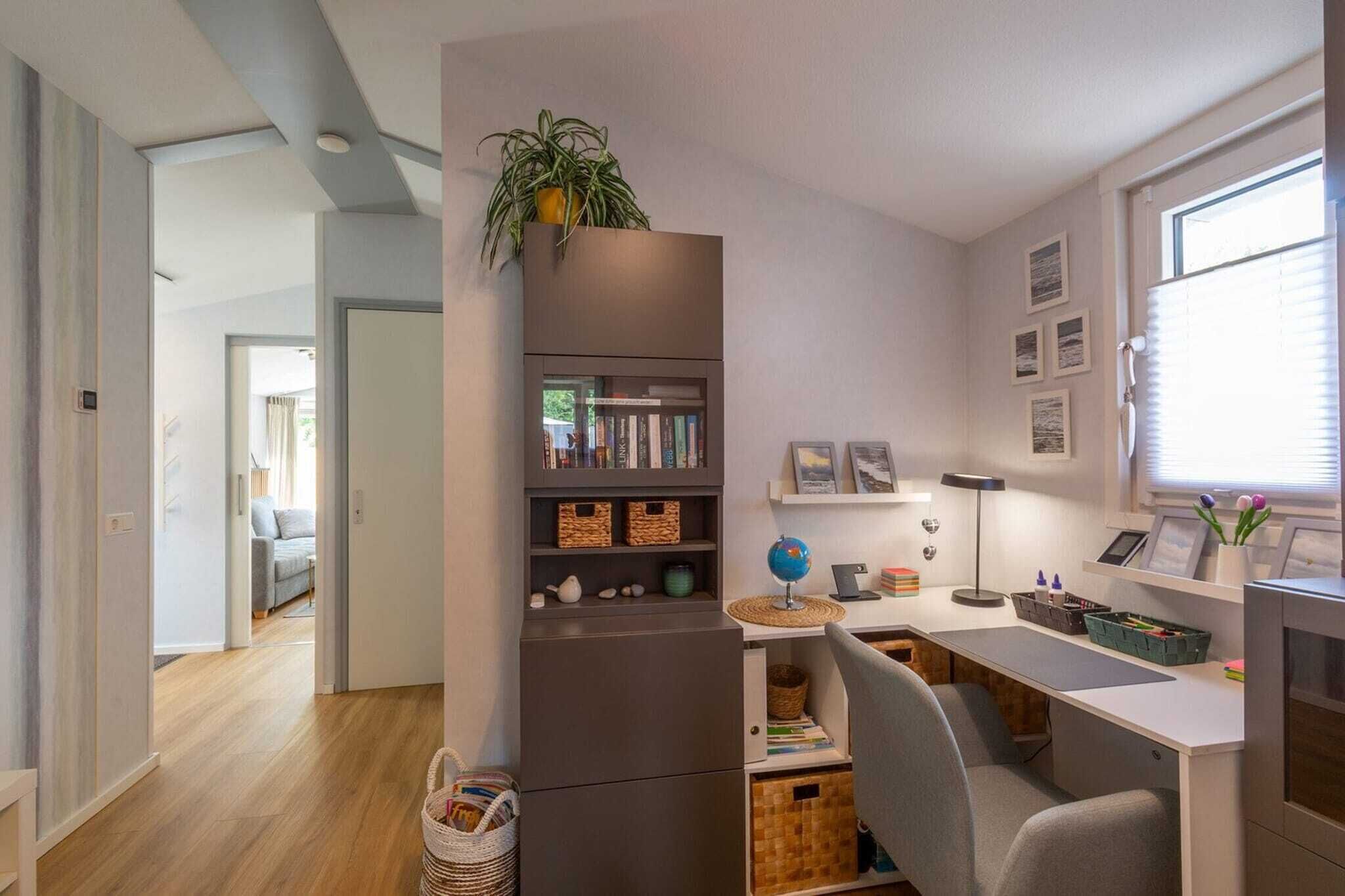 Un espace de vie moderne et compact, comprenant un coin cuisine, un bureau avec un ordinateur et une bibliothèque.