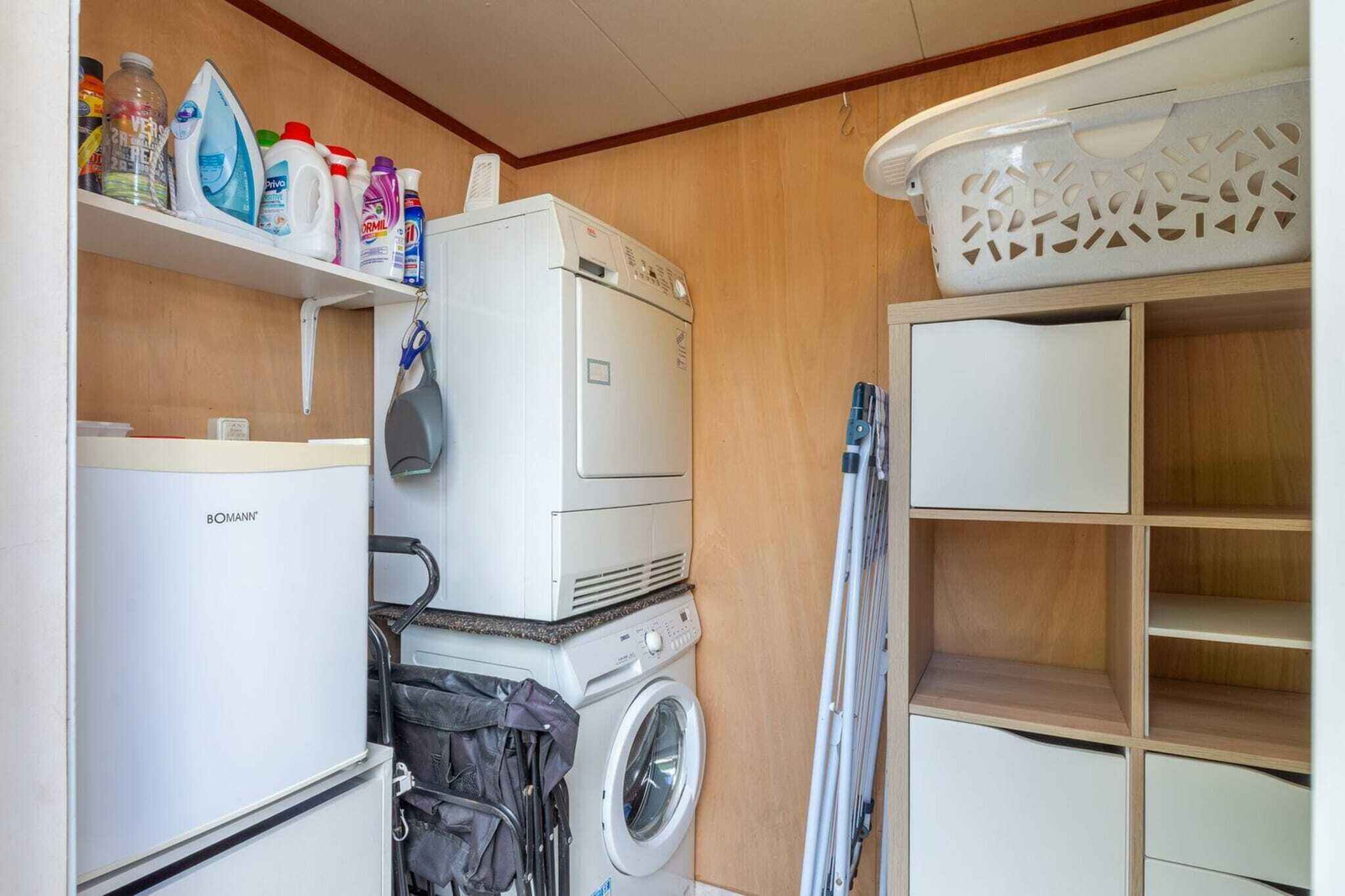 A laundry room with a washing machine, dryer, ironing board, and shelves with cleaning supplies.