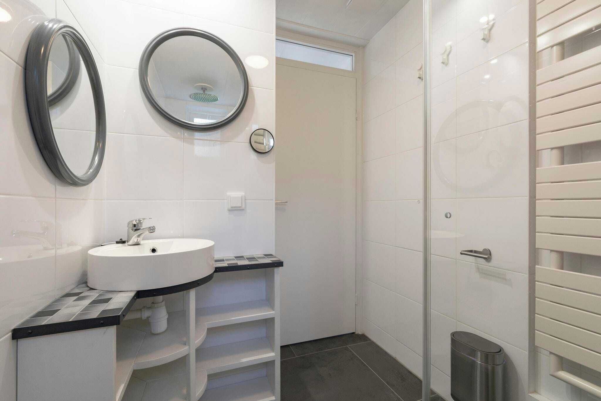 Une salle de bain moderne avec un lavabo blanc, deux miroirs et une douche dotée d’une porte en verre.