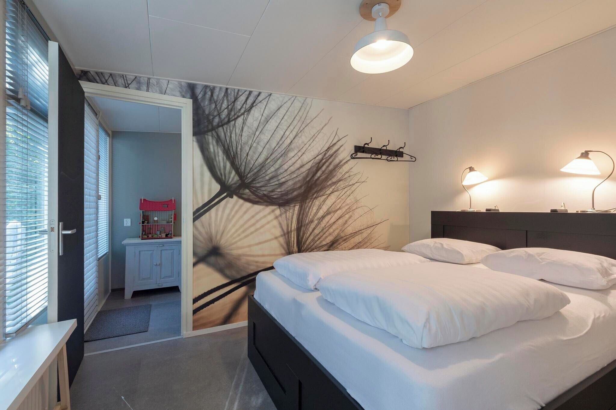 A bedroom with a bed, bedside lamps, a wall art piece, and a door leading to a bathroom.