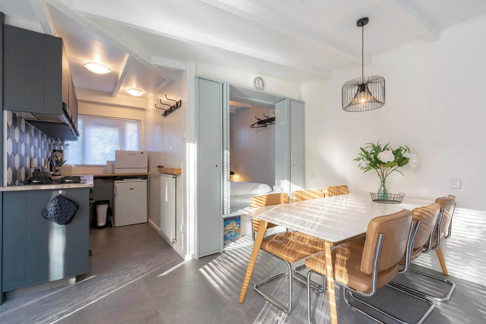 A modern kitchen with grey cabinets, a built-in oven, and a dining area with a white table and brown chairs.