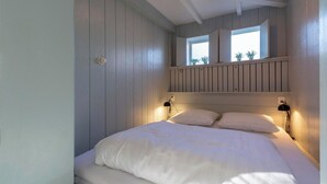Un dormitorio con una cama, dos lámparas de noche, una ventana con plantas y un cabecero de madera.