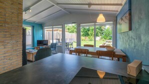 A modern kitchen with a large island, white cabinets, and a view of the backyard. - Garnekuul 56 holiday home for family (Callantsoog)