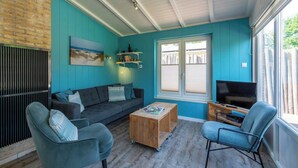A cozy living room with a blue wall, a wooden coffee table, a grey sofa, and a television. - Garnekuul 56 holiday home for family (Callantsoog)