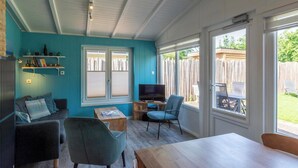 A cozy room with a blue wall, a wooden table, a TV, and a chair. - Garnekuul 56 holiday home for family (Callantsoog)