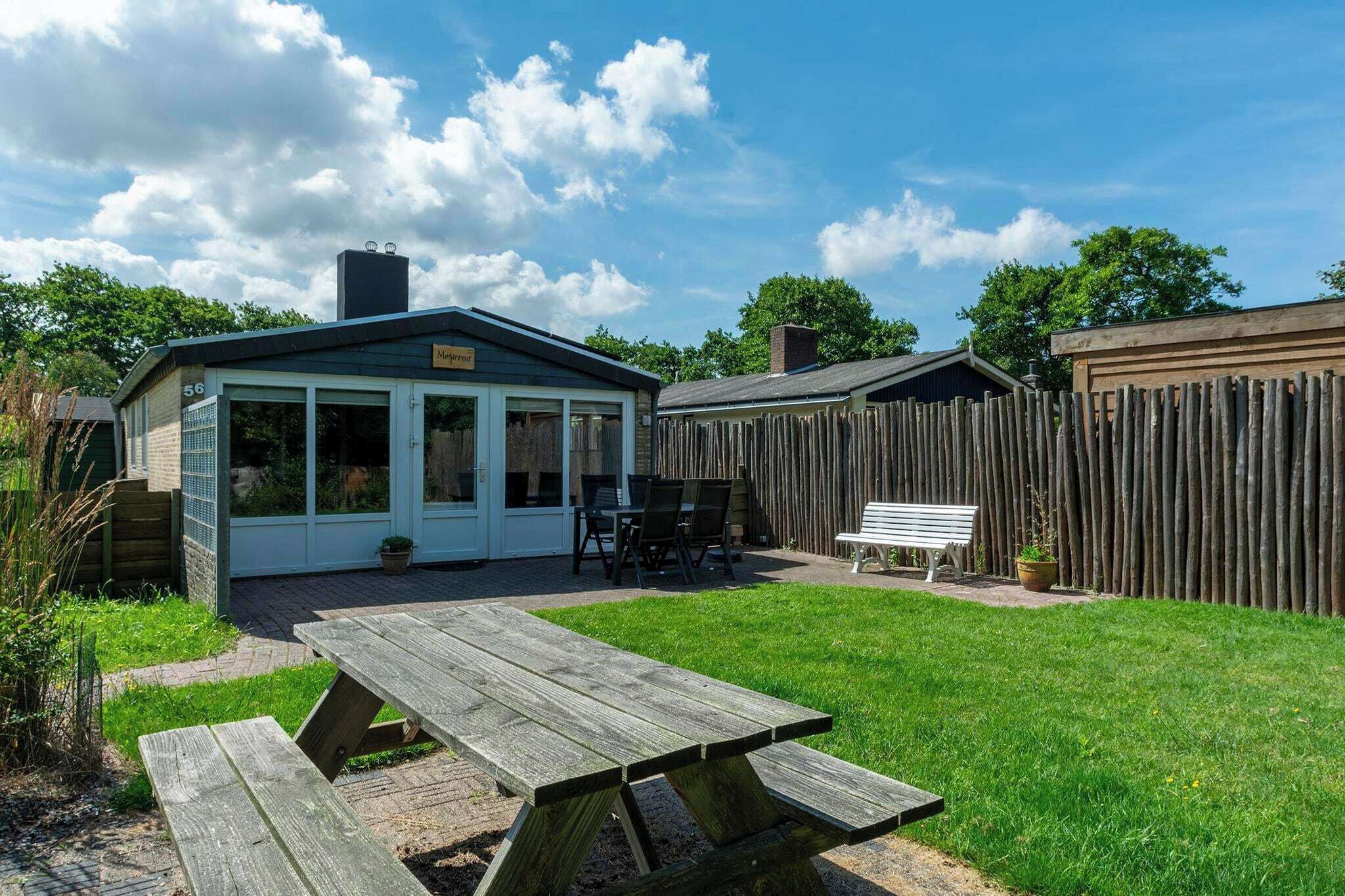 A backyard with a wooden picnic table, a covered patio area, and a fenced yard.