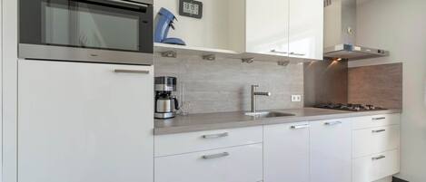 A modern kitchen with white cabinets, a stainless steel oven, a coffee maker, and a sink.