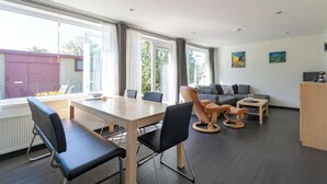 Ein modernes Wohnzimmer mit einem Holzes Esstisch, schwarzen Stühlen, einem grauen Sofa und einem Couchtisch aus Holz.