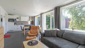 Ein modernes Wohnzimmer mit einem grauen Sofa, einem Ledersessel und einem Essbereich mit Tisch und Stühlen.