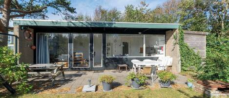 A modern house with a patio, outdoor seating, and potted plants.