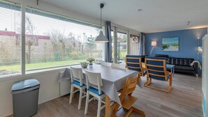 A dining area with a table and chairs, a trash bin, and a window with blinds.