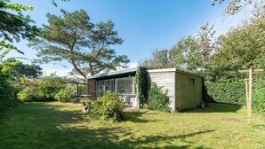 A small wooden cabin with a glass enclosure, surrounded by a lush garden and trees.