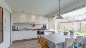 A modern kitchen with white cabinets, a dining table with chairs, and a large window with blinds.