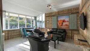 A living room with a large window, a black leather sofa, a coffee table, and a TV mounted on the wall.