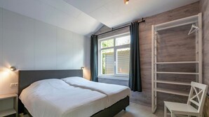 A bedroom with a bed, a nightstand, a chair, a wardrobe, and a window with curtains.