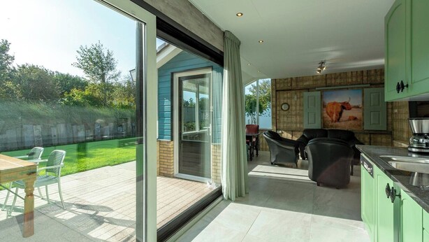 A modern kitchen with green cabinets, a dining area with a table and chairs, and a sliding glass door leading to a patio with a lawn and chairs.