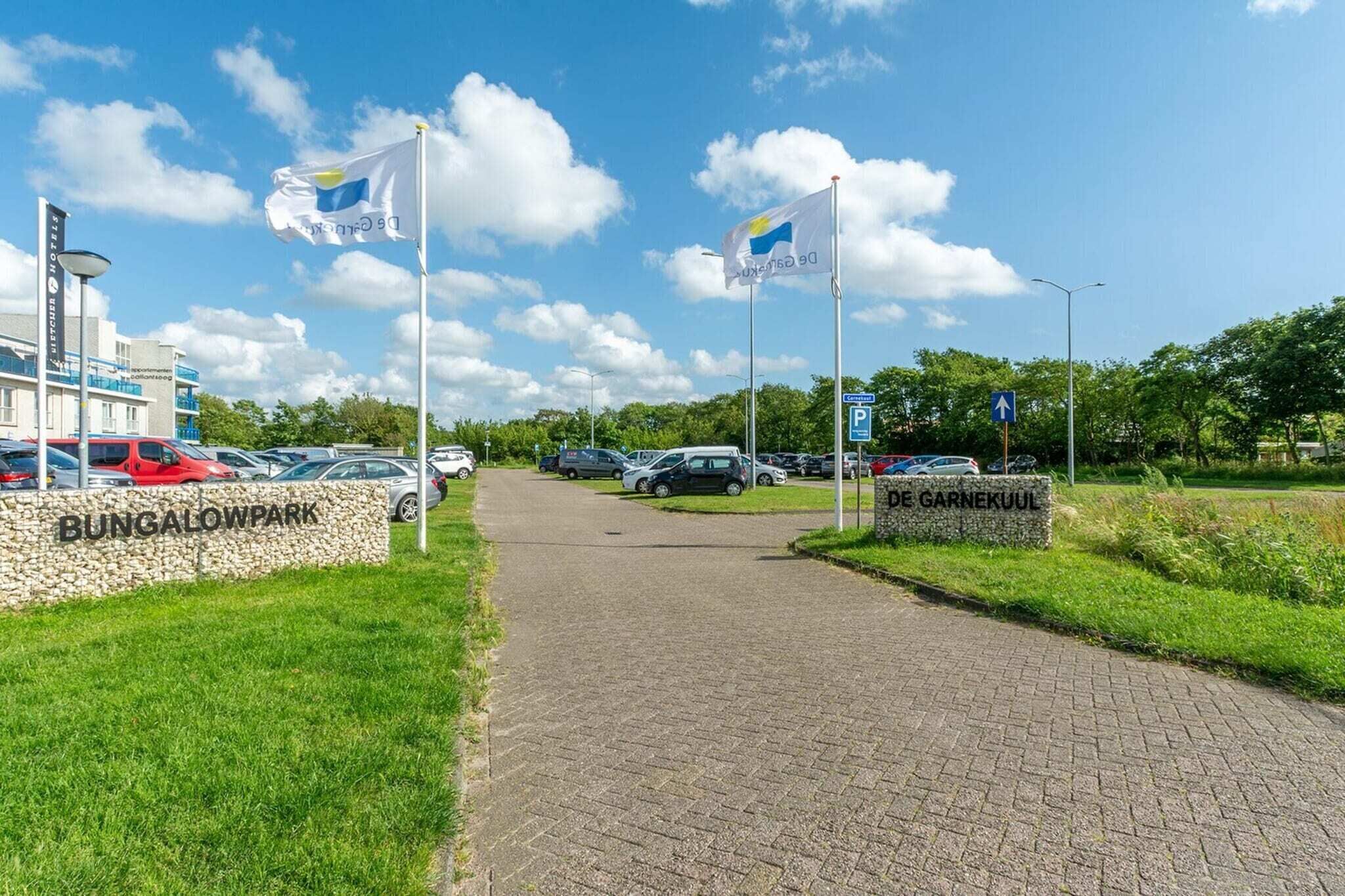 Een verhard pad leidt naar een bungalowpark, met een stenen muur waarop 'BUNGALOWPARK' staat.