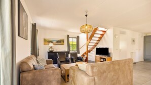 A modern living room with a sofa set, a dining table, a TV, and a staircase. - Villa with view over the park De Buitenplaats (Callantsoog)