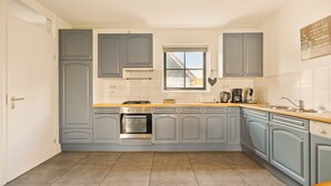 A kitchen with grey cabinets, a window, a stove, and a coffee maker. - Villa with view over the park De Buitenplaats (Callantsoog)