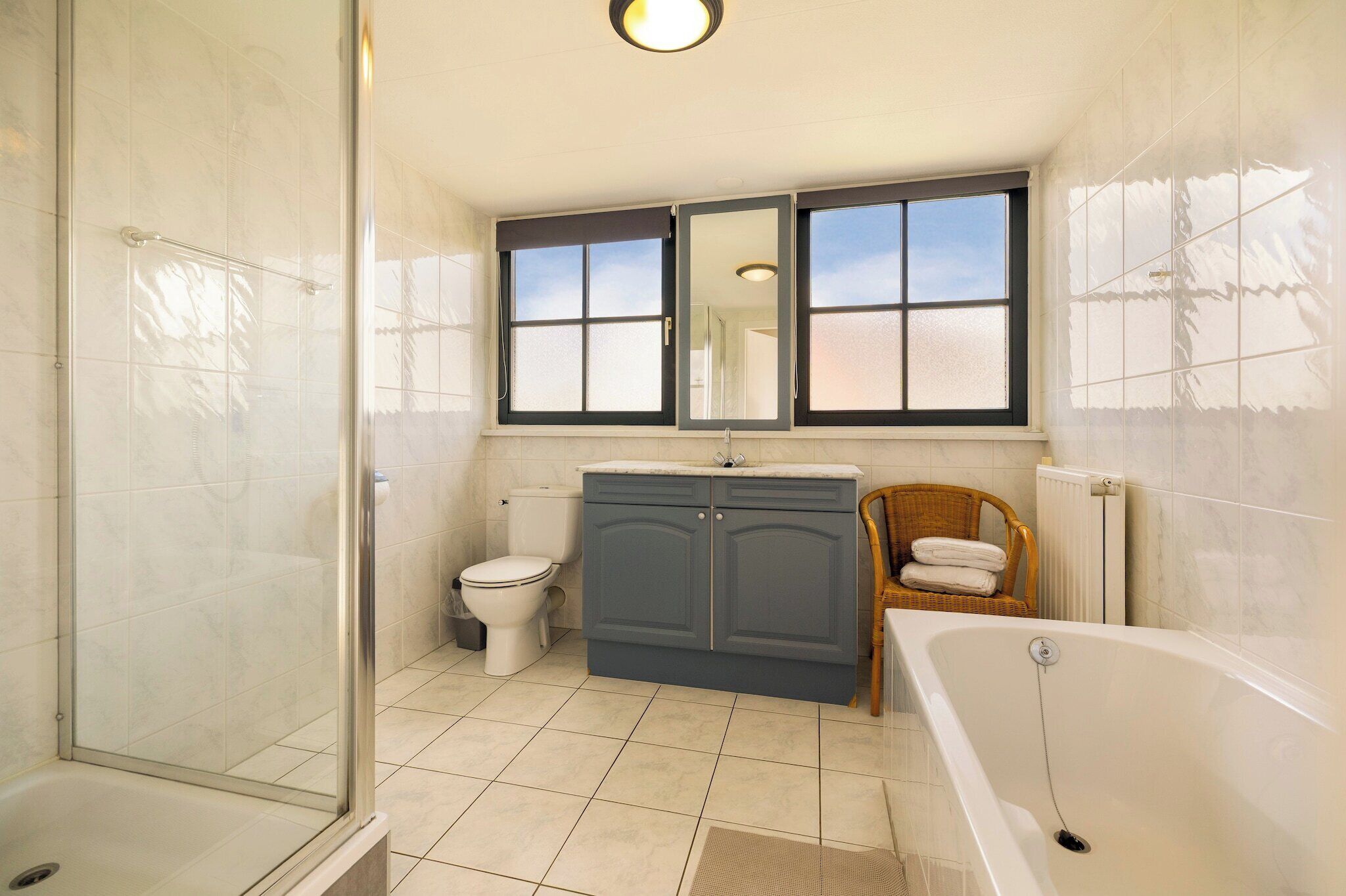 A bathroom with a glass shower enclosure, a toilet, a sink with a mirror above, and a bathtub.