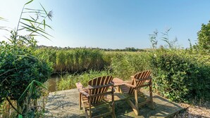 A wooden deck with two chairs and a table overlooking a natural landscape with water and vegetation. - De Buitenplaats 7 villa with dune views (Callantsoog)