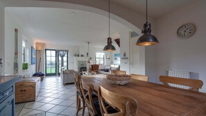 A spacious kitchen with a large wooden table, hanging pendant lights, and a view to the dining area. - De Buitenplaats 7 villa with dune views (Callantsoog)