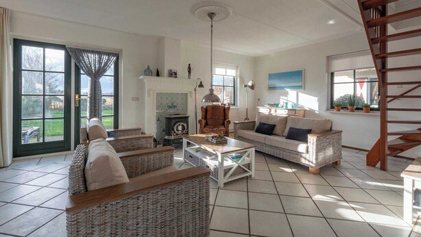 A spacious living room with wicker furniture, a fireplace, and a wooden staircase. - De Buitenplaats 7 villa with dune views (Callantsoog)