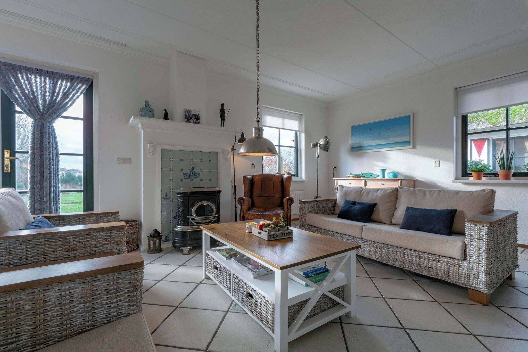 Een gezellige woonkamer met rieten meubels, een open haard en een groot raam met gordijnen.