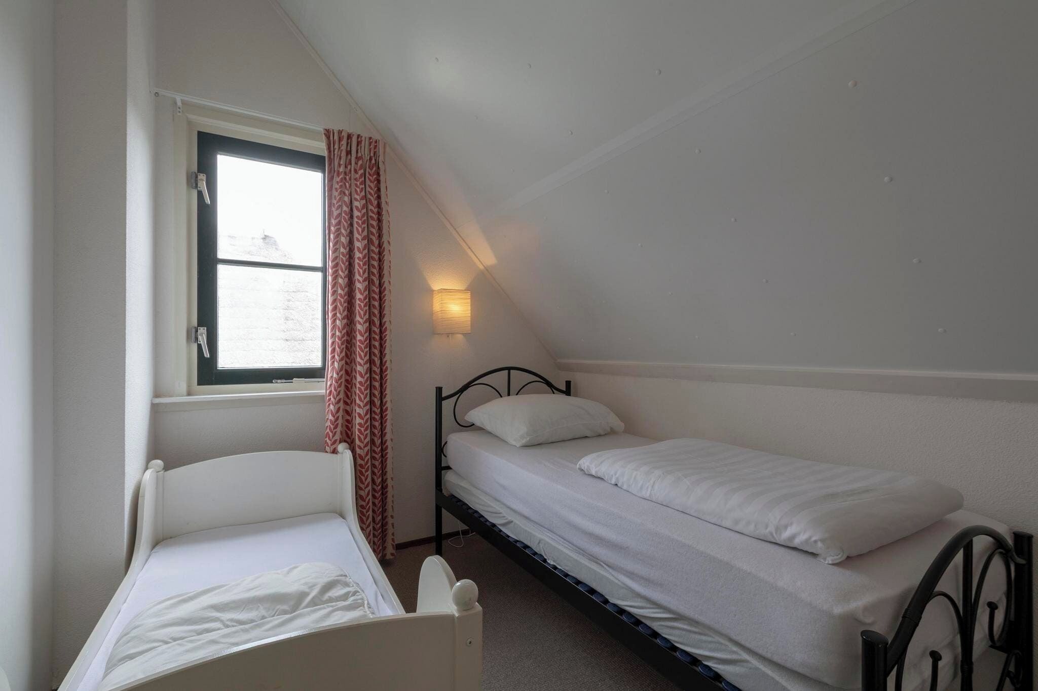 Una habitación pequeña, individual, con dos camas, una ventana con cortinas y una lámpara en la pared.