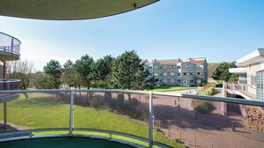 Blick vom Balkon auf einen Pool, mit Blick auf eine Rasenfläche und ein Gebäude mit mehreren Fenstern und Balkonen.