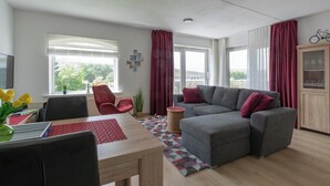 Ein modernes Wohnzimmer mit grauem Sofa, roten Stühlen, einem Holzessttisch und einem roten Teppich.