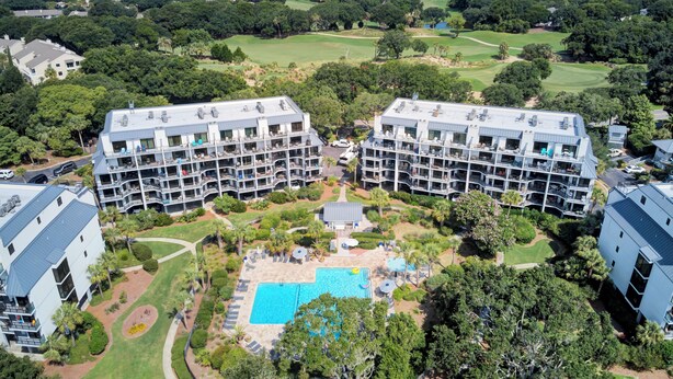 A large hotel with multiple floors, a central courtyard with a swimming pool, and surrounding lush greenery. - 123D Shipwatch by AvantStay | Beach Access + Pool (Isle Of Palms)